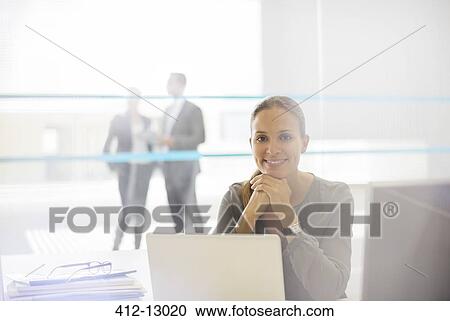 Stock Image - Portrait of confident businesswoman at laptop in office. Fotosearch