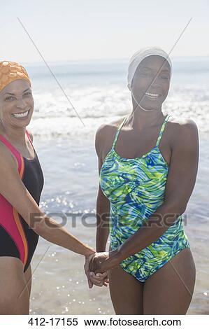 Stock Photography - Portrait of happy lesbian couple holding hands on beach. Fotosearch