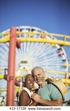 Portrait of happy senior couple hugging at amusement park View Large Photo Image Stock Photo - Portrait of happy senior couple hugging at amusement park. Fotosearch
