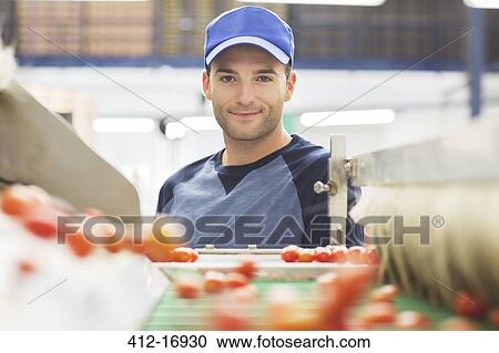 Stock Image - Portrait of worker at conveyor belt in food processing plant. Fotosearch