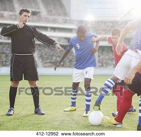 Stock Image - Referee whistling at soccer players on field. Fotosearch