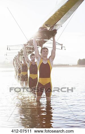 Stock Image - Rowing team carrying scull overhead in lake. Fotosearch