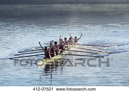 Stock Image - Rowing team celebrating in scull on lake. Fotosearch
