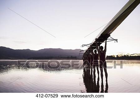 Rowing team entering lake at dawn with scull overhead View Large Photo Image Stock Photo - Rowing team entering lake at dawn with scull overhead . Fotosearch