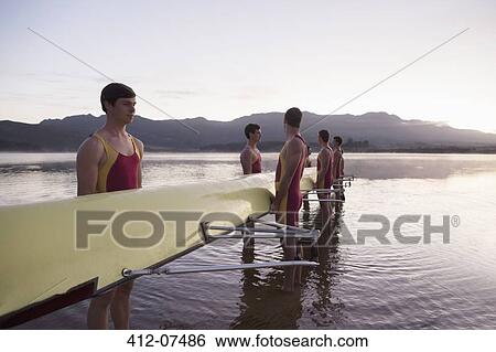 Stock Photograph - Rowing team holding scull in lake at dawn. Fotosearch