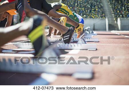 Stock Image - Runners poised at starting blocks on track. Fotosearch