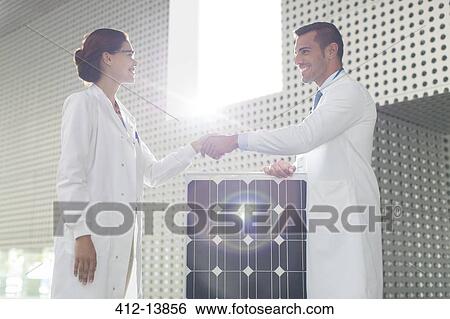 Stock Photograph - Scientists handshaking at solar panel in laboratory. Fotosearch