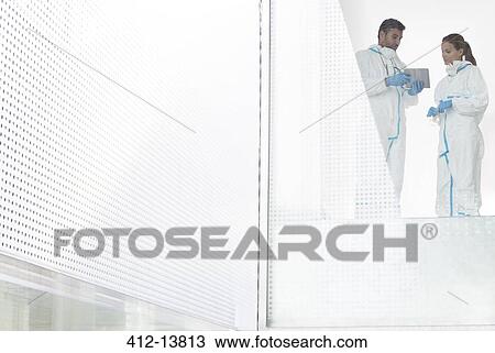 Stock Image - Scientists in clean suits using digital tablet. Fotosearch
