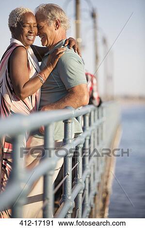 Stock Image - Senior couple hugging on pier. Fotosearch