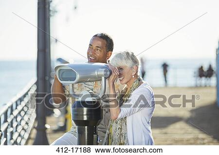 Senior couple using coin-operated binoculars on pier View Large Photo Image Stock Photo - Senior couple using coin-operated binoculars on pier. Fotosearch