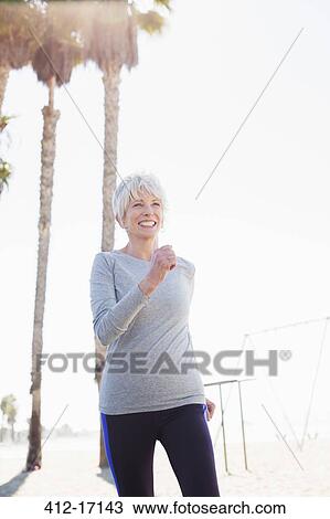 Stock Image - Senior woman power walking on beach boardwalk. Fotosearch