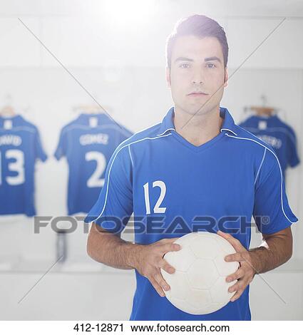 Stock Image - Soccer player holding ball in locker room. Fotosearch