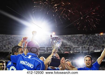 Stock Image - Soccer team celebrating with trophy on field. Fotosearch