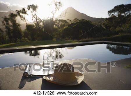 Stock Photo - Sun hat, water glasses and magazine on lounge chairs at poolside. Fotosearch