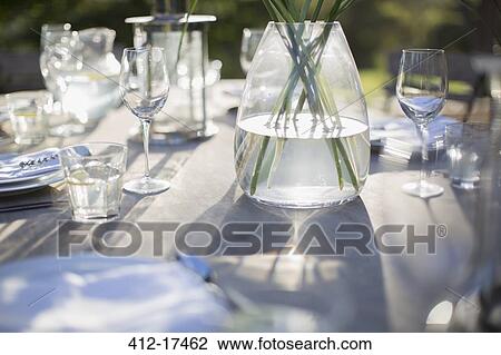 Stock Image - Vase and place settings on sunny patio table. Fotosearch