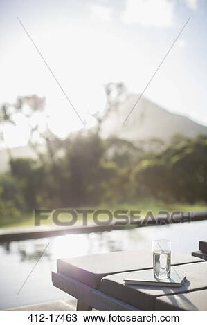 Water glass and book on lounge chair at sunny poolside View Large Photo Image Stock Image - Water glass and book on lounge chair at sunny poolside. Fotosearch