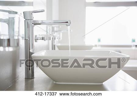 Stock Photo - Water pouring from faucet in modern bathroom. Fotosearch