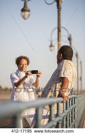 Stock Photography - Woman photographing man on pier. Fotosearch
