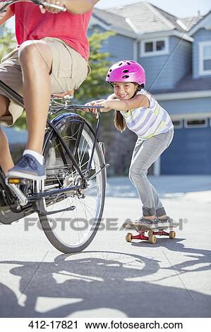Daughter on skateboard pushing father on bicycle View Large Photo Image Stock Image - Daughter on skateboard pushing father on bicycle. Fotosearch