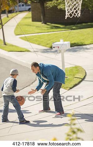 Stock Photo - Father and son playing basketball in sunny driveway. Fotosearch