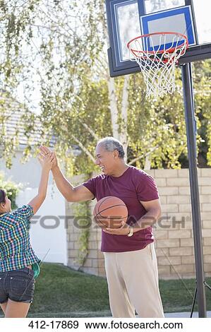 Grandfather and granddaughter high fiving at basketball hoop View Large Photo Image Stock Photo - Grandfather and granddaughter high fiving at basketball hoop. Fotosearch