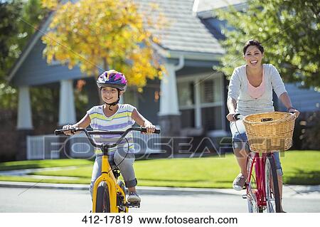 Stock Photo - Mother and daughter riding bicycles in sunny street. Fotosearch