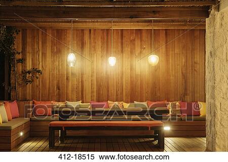 Stock Photography - Pendant lights illuminated over patio bench with cushions. Fotosearch