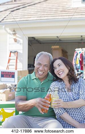 Portrait of happy couple toasting soda bottles at garage sale View Large Photo Image Stock Photograph - Portrait of happy couple toasting soda bottles at garage sale. Fotosearch