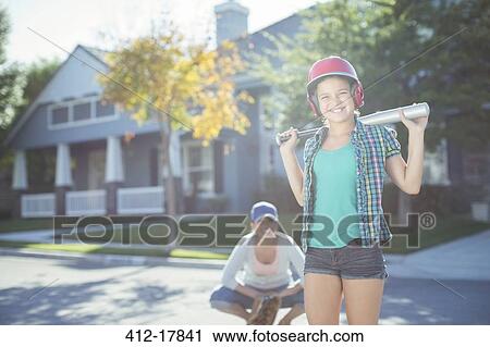 Stock Image - Portrait of mother and daughter playing baseball in street. Fotosearch
