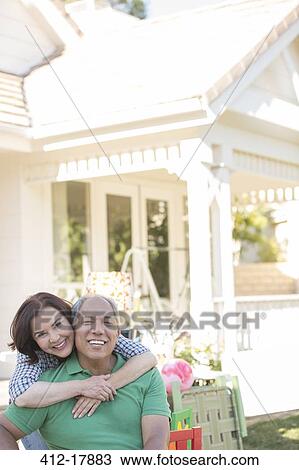 Stock Image - Portrait of smiling couple hugging outside garage sale. Fotosearch