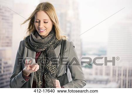 Stock Image - Smiling businesswoman using cell phone in urban window. Fotosearch