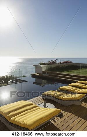 Stock Photograph - Sun shining over lounge chairs at poolside overlooking ocean. Fotosearch
