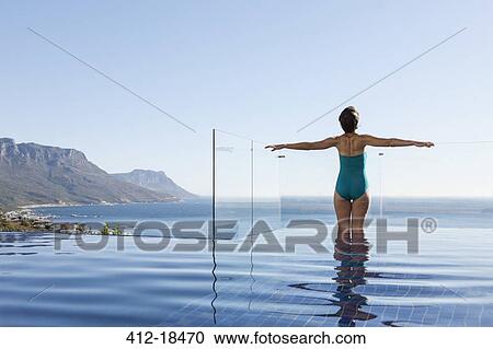 Stock Image - Woman basking in infinity pool overlooking ocean. Fotosearch