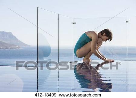 Stock Photo - Woman crouching over infinity pool with ocean view. Fotosearch