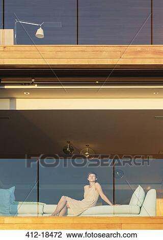Stock Image - Woman sitting on sunny luxury balcony. Fotosearch