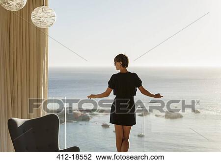 Stock Image - Woman standing at balcony railing overlooking ocean. Fotosearch