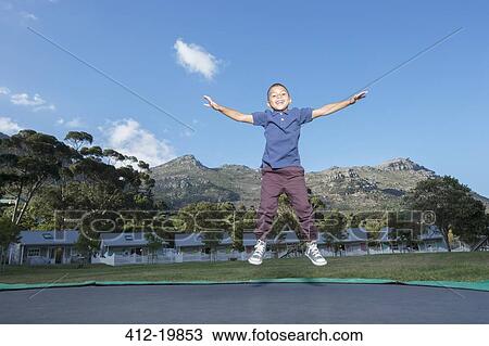 Stock Image - Boy jumping on trampoline outdoors. Fotosearch