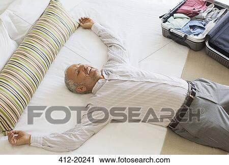 Businessman laying on bed in hotel room View Large Photo Image Stock Image - Businessman laying on bed in hotel room. Fotosearch