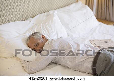Businessman laying on bed in hotel room View Large Photo Image Stock Image - Businessman laying on bed in hotel room. Fotosearch