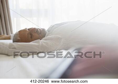 Businessman laying on bed in hotel room View Large Photo Image Stock Photograph - Businessman laying on bed in hotel room. Fotosearch