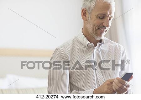 Businessman using cell phone in hotel room View Large Photo Image Picture - Businessman using cell phone in hotel room. Fotosearch