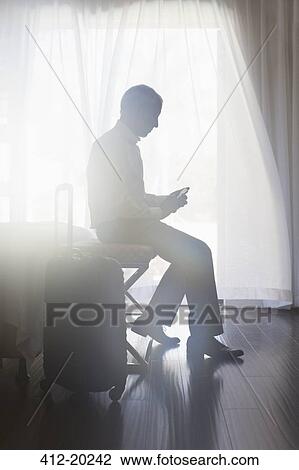 Stock Image - Businessman using cell phone in hotel room. Fotosearch