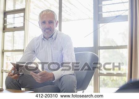 Businessman using digital tablet in living room View Large Photo Image Stock Image - Businessman using digital tablet in living room. Fotosearch