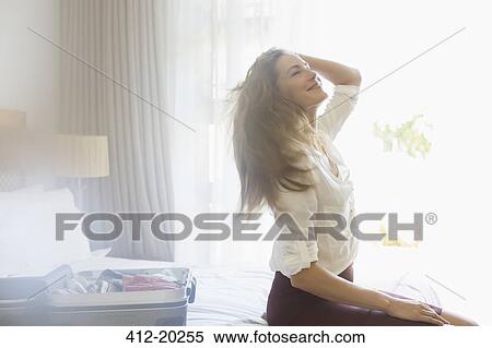 Stock Photography - Businesswoman sitting on bed in hotel room. Fotosearch