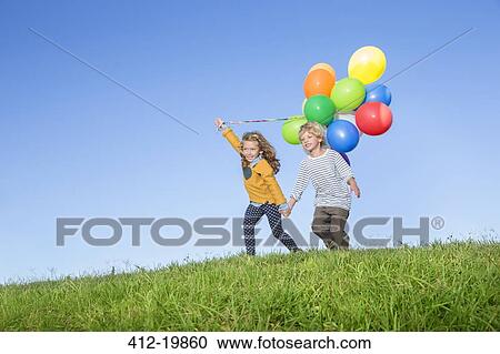 Stock Image - Children with bunch of balloons on grassy hill. Fotosearch