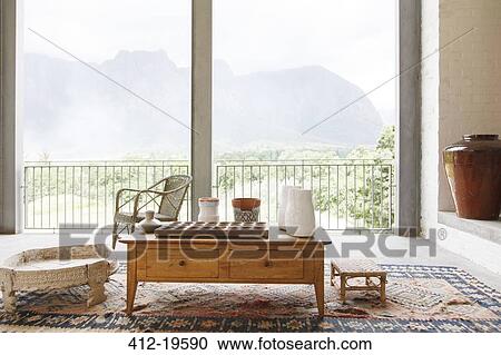 Stock Image - Coffee table in living room overlooking landscape. Fotosearch