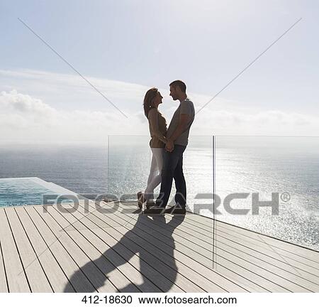 Stock Image - Couple on modern balcony overlooking ocean. Fotosearch