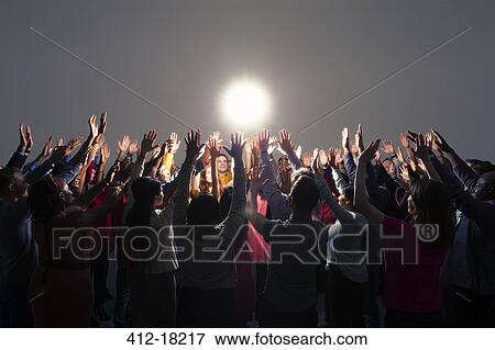 Diverse crowd with arms raised around bright light View Large Photo Image Stock Photo - Diverse crowd with arms raised around bright light. Fotosearch