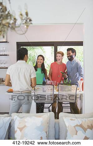Friends laughing together in kitchen View Large Photo Image Stock Image - Friends laughing together in kitchen. Fotosearch