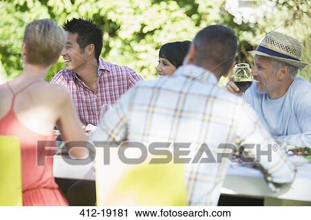 Friends relaxing at table outdoors View Large Photo Image Stock Image - Friends relaxing at table outdoors. Fotosearch